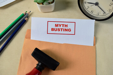 Red Handle Rubber Stamper and Myth busting text above Brown envelope isolated on wooden background