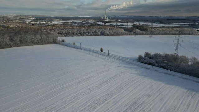 drone footage of snowy fields, with a power plant on the horizon.