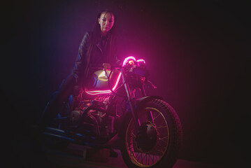 Plakat Girl a motorbiker near the old motorcycle in the neon lights.