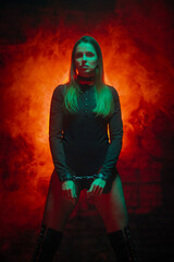 Beautiful girl in bodysuit with hands in handcuffs posing on the red light smoke background.