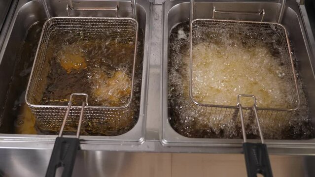 Close-up of French fries and nuggets in a deep fryer with boiling oil. Delicious French fries are cooked in a deep fryer in the kitchen. Potato chips and nuggets fried in a steel sieve in the kitchen.