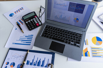 Laptop and financial graph documents on businessman's desk with wooden toys following steps of increasing graph. Ideas for the process of successful business growth.