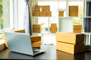 Parcel boxes on shelves and colored shopping bags near laptop on table. SME business in online shopping at home.