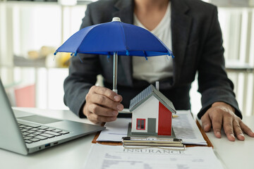 Blue umbrella covering a house model on a wooden table Property insurance, mortgage insurance...