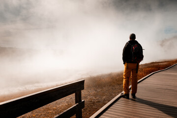 Male tourist standing on a boardwlak in the Yellowstone National Park and enjoying the view of a...