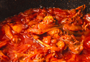 Chicken meat is stewed in tomato in a frying pan