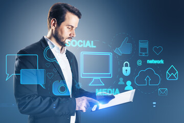 Attractive young european businessman using tablet with creative social media interface with emails, speech bubbles, mobile internet, cloud computing and other icons on blurry background.