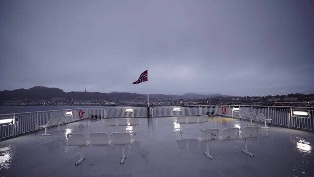 waving norwegian flag on wet aft deck on the ferry during rain with mountains and city of bodo on background