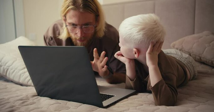 A happy albino boy with white hair looks at his father while watching an educational film and asks him a question. The man answers his boy and tries to clarify all his questions
