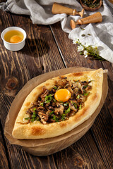 Adjarian khachapuri adorned with mushrooms and a bright egg yolk, served on a rustic wood backdrop