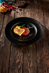 Pan-fried cheese with berry sauce, served on a black plate with a rustic wooden background