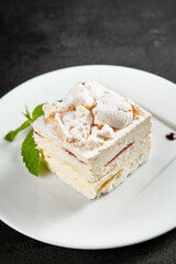 Delicate meringue cake with creamy cheese filling, garnished with a sprig of mint on a white plate