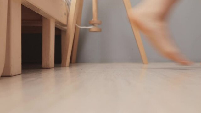 Side view of unrecognizable unknown barefoot woman getting out of bed on floor in bedroom in morning after waking up walking in room