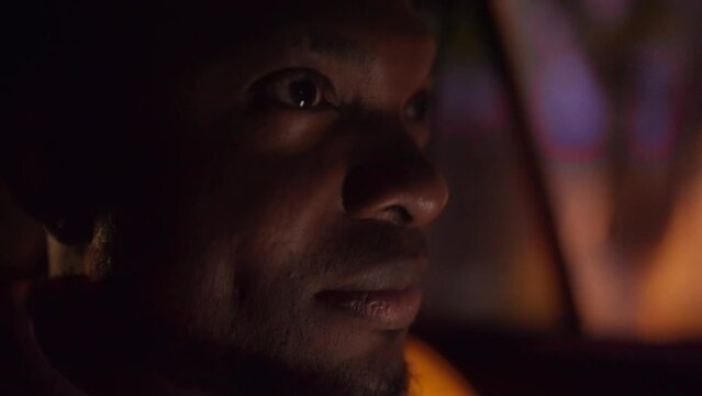 Close up a man with Black skin and a beard rides through the evening city in the interior of a modern car looks and enjoys the views during his trip