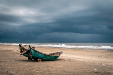 Fototapeta na wymiar Old wooden fishing boat on a beach against a backdrop of tumultuous grey clouds
