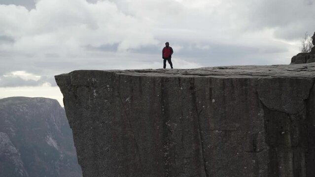 man hiker tourist standing on Preikestolen Pulpit Rock cliff and bends over during severe windy weather in norway in slow motion