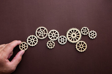 Hand holding wooden cog flowing process management.