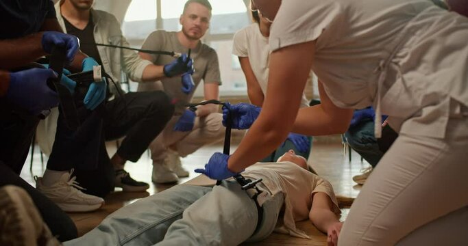 Close-up shooting: A professional nurse-girl in a white medical uniform demonstrates the technique of applying a medical tourniquet to a person's leg during a practical training in first aid