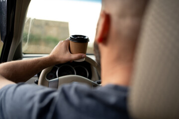 Taxi driver drinking takeaway coffee while driving his car while standing in traffic jam in the...