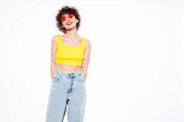 Young beautiful smiling female in trendy summer yellow tank top. Carefree woman posing near white...