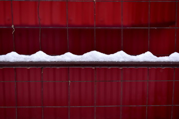 melting snow on a metal fence against a red wall