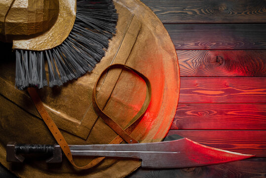 Ancient Spartan sword, helm and shield on the wooden table background concept. Top view.