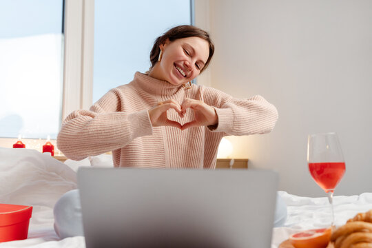 Beautiful smiling woman using laptop computer showing heart shape, drinking wine communication with boyfriend celebration Valentines day at home. Love, online dating concept - Powered by Adobe