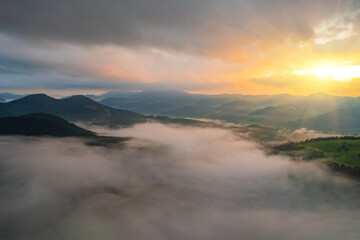 Amazing morning fog in the mountains. Beautiful sunrise light shines on the red beech forest. Drone panorama.