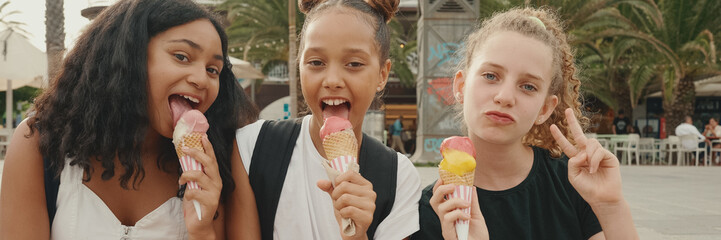 Laughing three girls friends pre-teenage are sitting on the waterfront testing ice cream. Three...