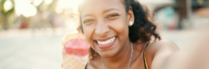 Closeup of smiling young woman with long curly hair with ice cream in her hands making a video call...