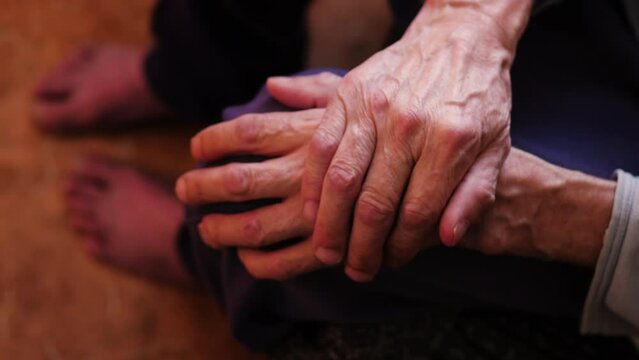 folded wrinkled veiny hands on the knees of an elderly man.senile dementia. an impersonal elderly man sits alone while inside.