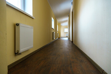 A long empty corridor in an office building. A new modern heating radiator on a white wall. Large double-glazed windows in a modern building.