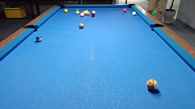 Player playing 8-ball pool billiards on blue table. Pool is a classification of cue sports.
