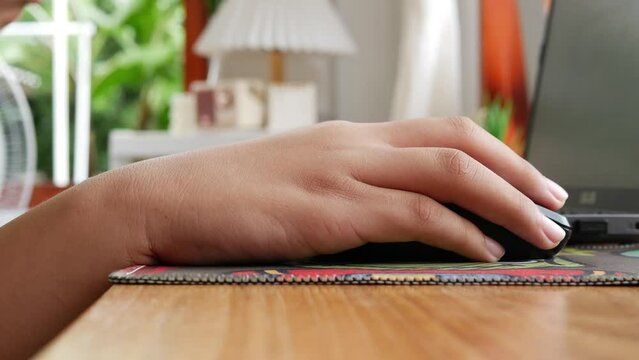 Close-up of boy's hands pressing computer mouse buttons, playing games and using laptop on table.