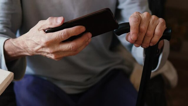 impersonal elderly man sitting with a walking cane watching video hosting using a smartphone holding it horizontally. daily life of old people
