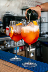 a bartender adding prosecco to a pair of Italian Aperol spritz cocktails 