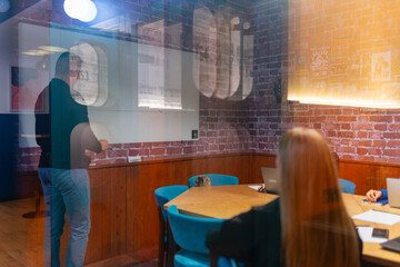 Young people meet in conference room with whiteboard behind glass wall. Professional workers...