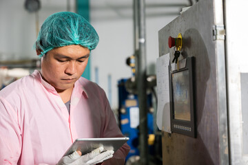 In beverage manufacturing a worker with a tablet supervises soda water filling while an engineer...