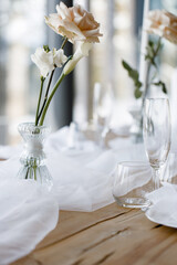 Banquet table setting in blue and white colors, top view. In the center of the table is a bouquet of bright exotic flowers on a drapery. Candles in gold candlesticks, plates with napkins, glasses.