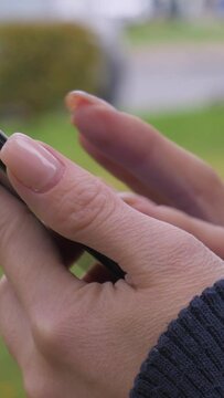 Woman hands with manicure are typing on black smartphone in the city street. Grass and cars lights on background. Close-up shot. 60 fps. Vertical Video