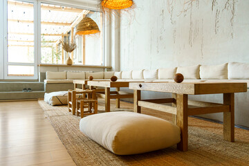 A spacious and cozy lounge with upholstered sofas, wooden tables and panoramic windows. A place to relax in a big house.