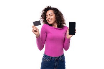 young curly brunette advertiser woman dressed in a lilac turtleneck holding a mobile phone and a plastic card