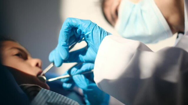 Compassionate female dentist assesses tooth decay in a young patient using a dental probe and angled mirror.