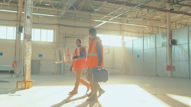 Wide side shot of three male colleagues crossing empty spacious room carrying ladder and tool boxes during workday
