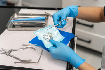 Close-up of the dentist's hand opens a sterile package with clamps. Dental instruments are on the...
