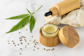 Hemp salve for joints and muscles in open glass wooden jar and relaxing CBD serum oil in bamboo dropper bottle as a complex in the treatment of the musculoskeletal system.