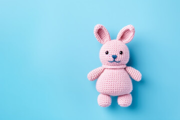 Knitted handmade pink rabbit on a blue background with copy space.	