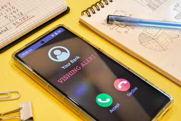 Smartphone screen showing phone call from bank with Vishing alert message. Phone call scam or phishing attack asking for bank details concept.