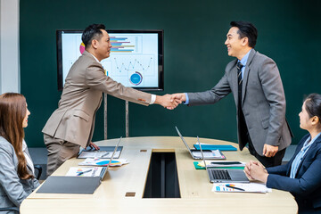 Businessman and middle aged businessman partners negotiate sign contract handshake at group meeting...