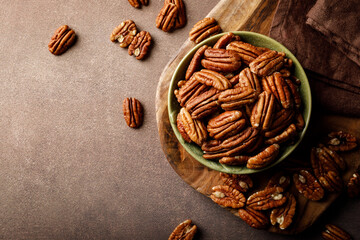 Pecan nuts in a bowl on a brown background, top view